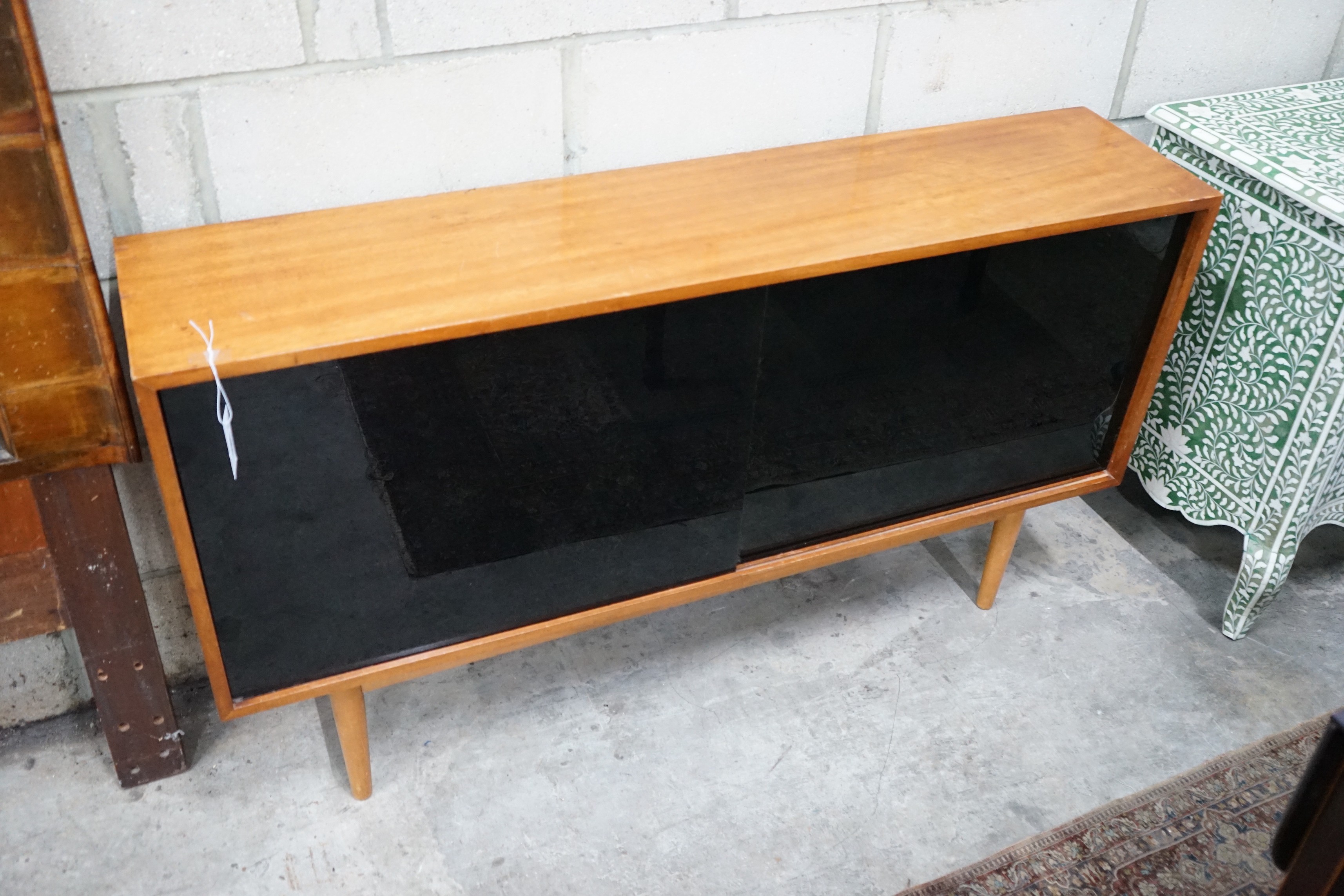 Robin Day for Hille, a teak and black glass sliding door side cabinet, width 137cms, depth 30cms height 76cms.